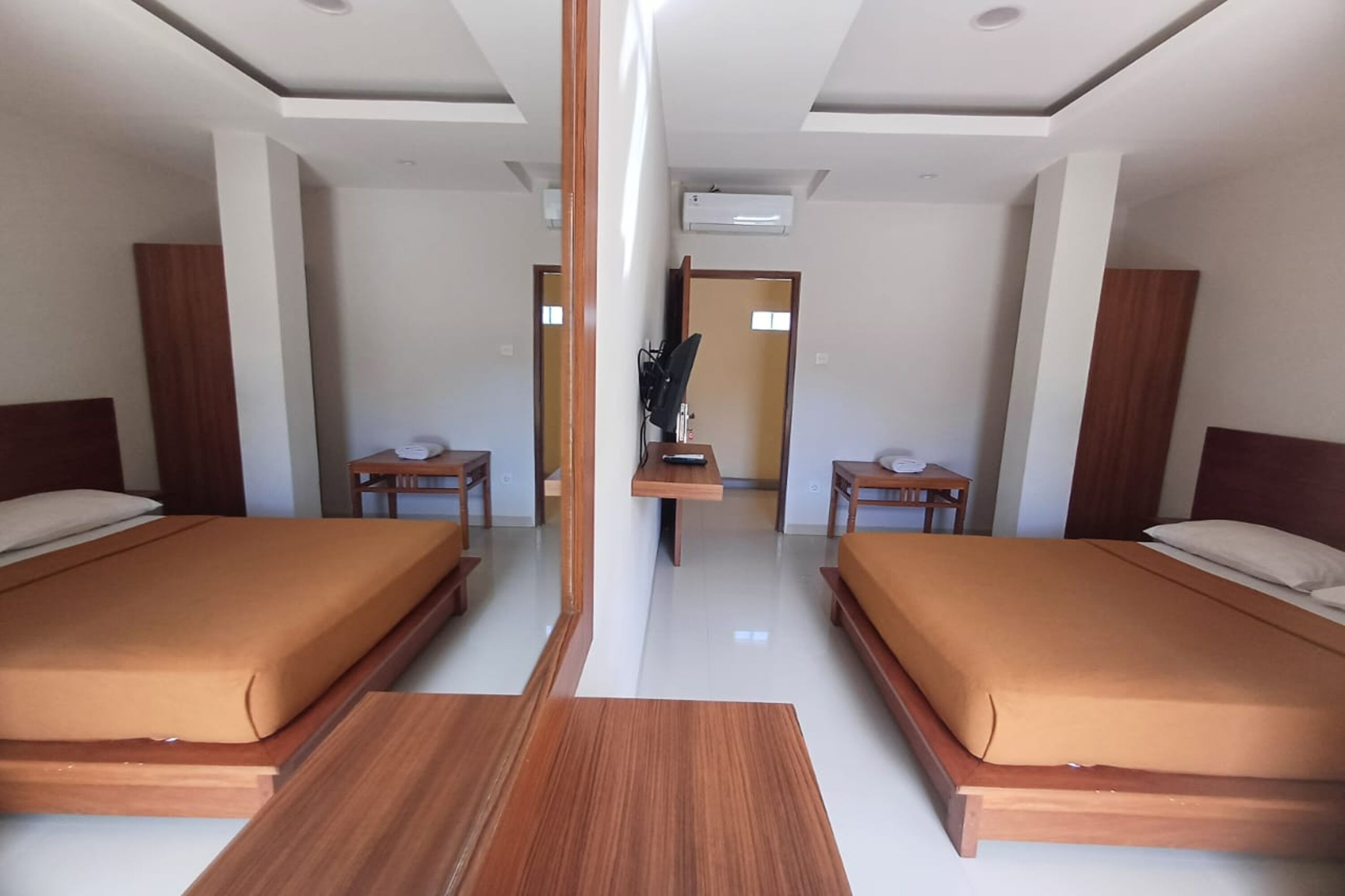 A hotel room with two beds, a wooden floor, a mirror, and a desk with a chair.
