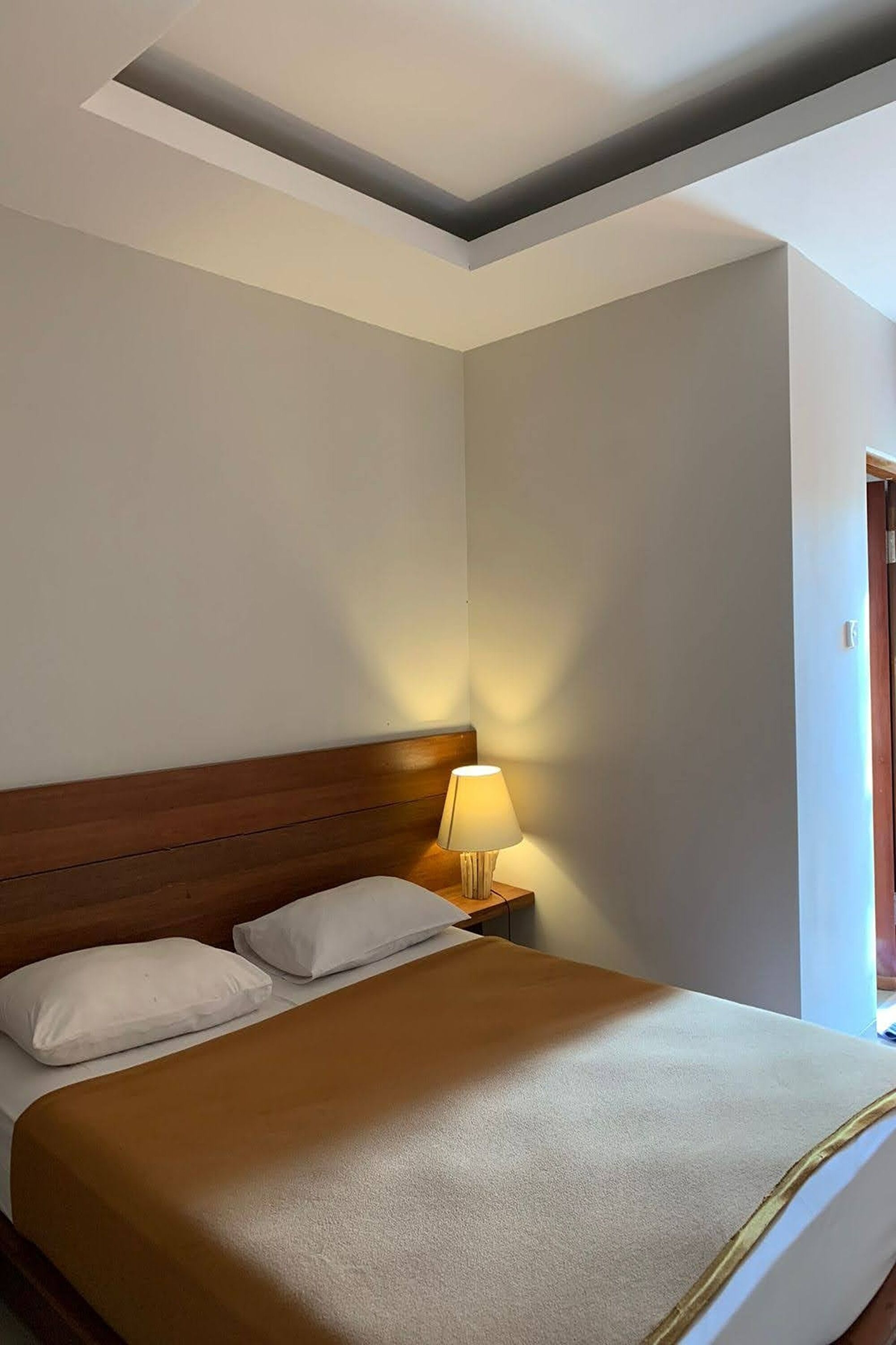 A neatly made bed with a wooden headboard, a bedside lamp, and a view of a door.