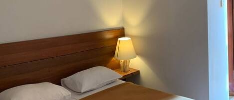 A neatly made bed with a wooden headboard, a bedside lamp, and a view of a door.