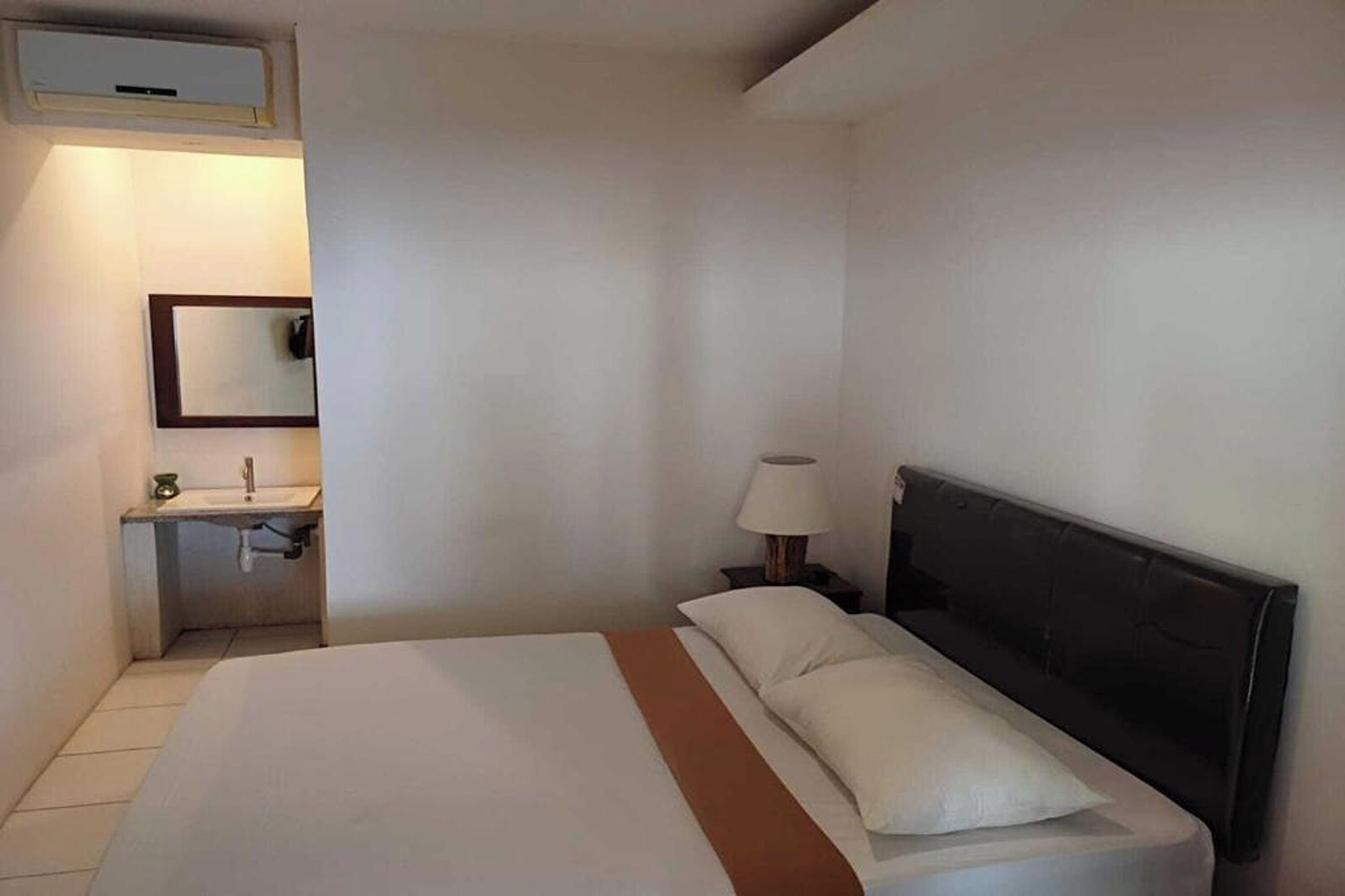 A hotel room with a bed, a nightstand, a lamp, a mirror, and a bathroom with a sink and towel rack.