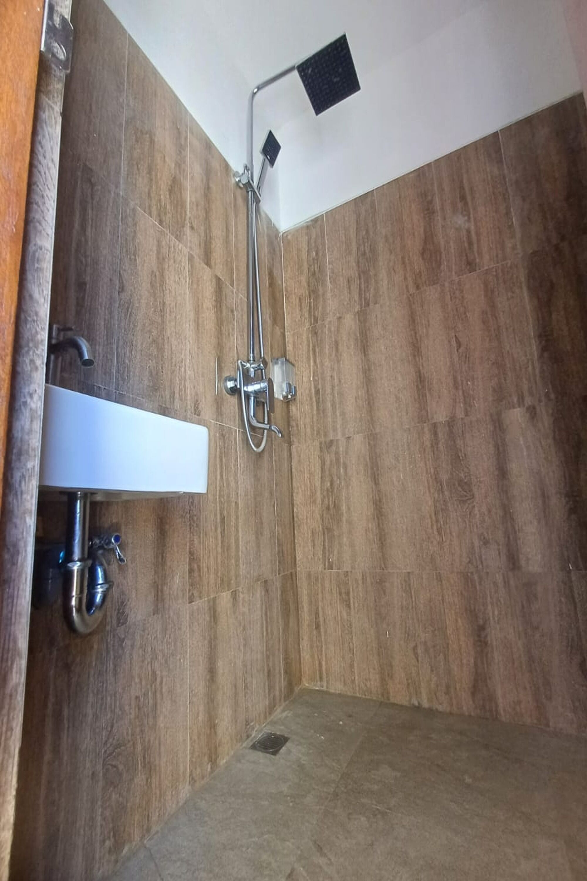 A bathroom with wooden walls, a white sink, and a shower with a handheld showerhead.