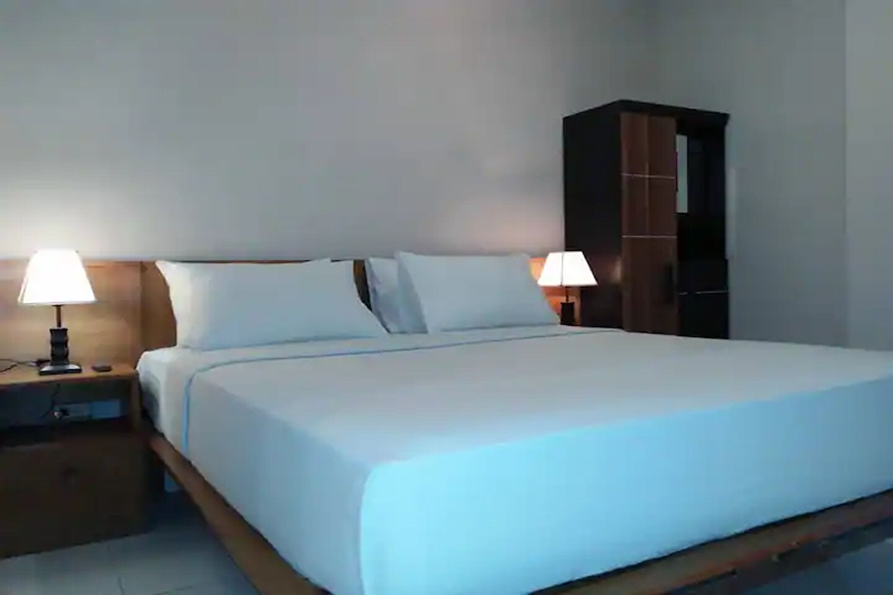 A neatly made bed with white linens, two bedside lamps, and a wooden nightstand.