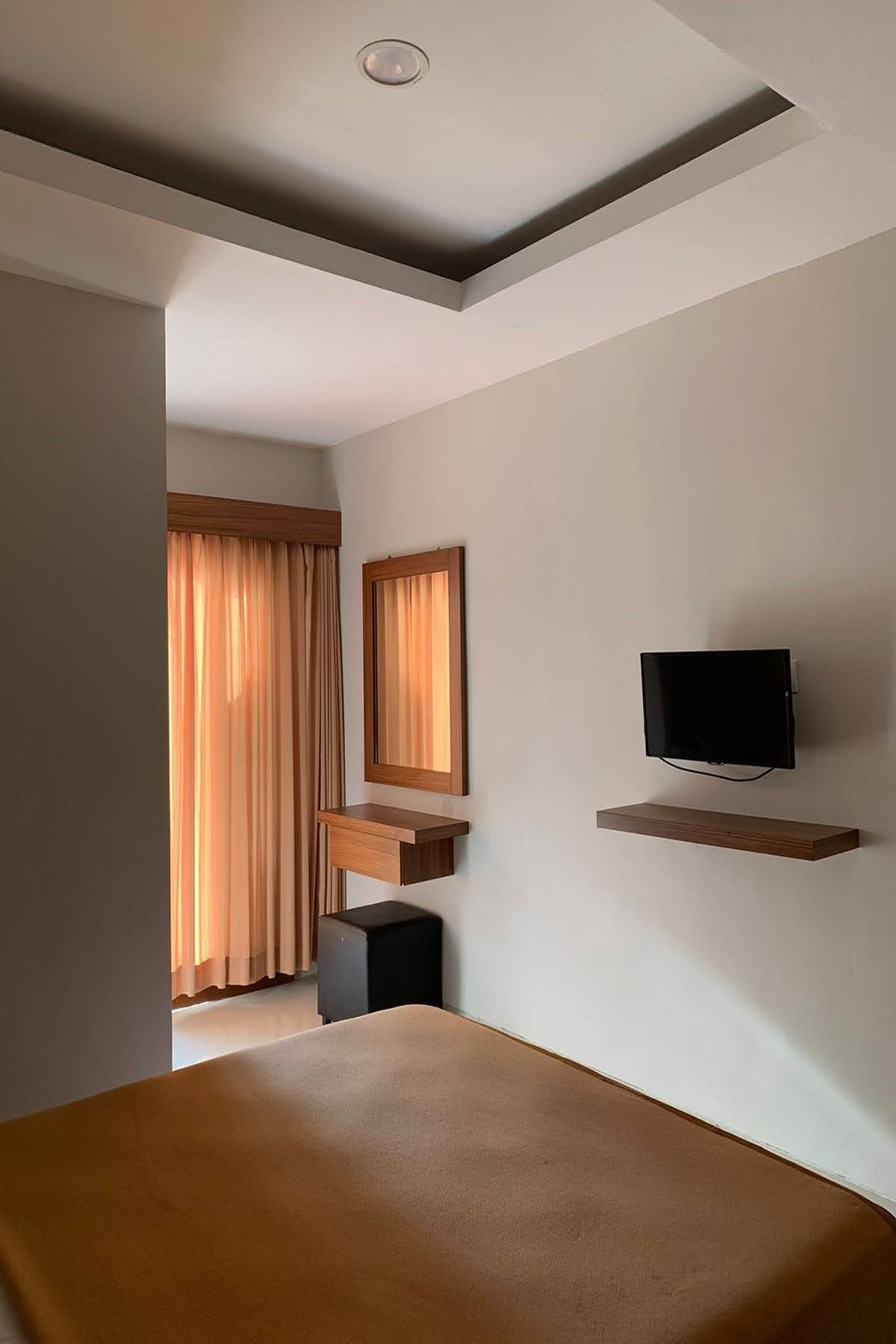 A modern hotel room with a bed, a TV mounted on the wall, and a small desk area.