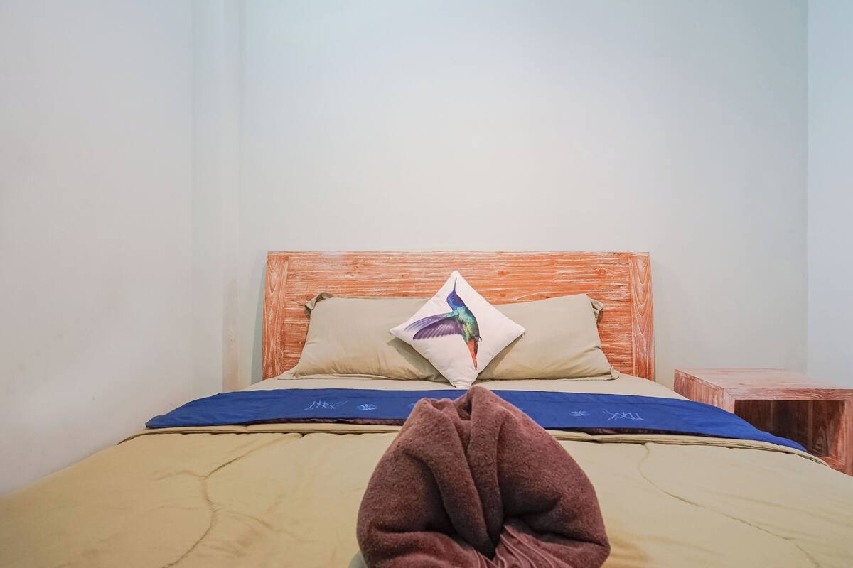 A bed with a wooden headboard, two pillows, a blue blanket, and a brown blanket.
