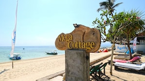A wooden sign reading "Mega Cottage" on a beach with a boat in the water and lounge chairs nearby. - Mega Cottages (Lembongan Island)