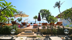 A beachside lounge area with outdoor seating, a view of the sea, and palm trees. - Mega Cottages (Lembongan Island)