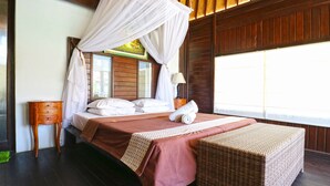 A bedroom with a bed, bedside table, and a wicker bench. - Mega Cottages (Lembongan Island)