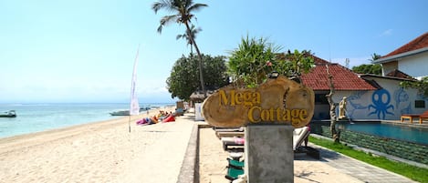 Un cartelito junto a la playa anuncia 'Mega Cottage', con piscina y un mural de un pulpo en la fachada.