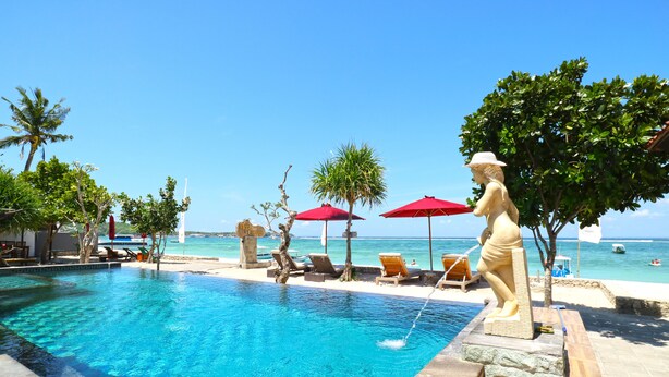 A clear blue pool with lounge chairs and umbrellas, surrounded by trees and a view of the ocean. - Mega Cottages (Lembongan Island)