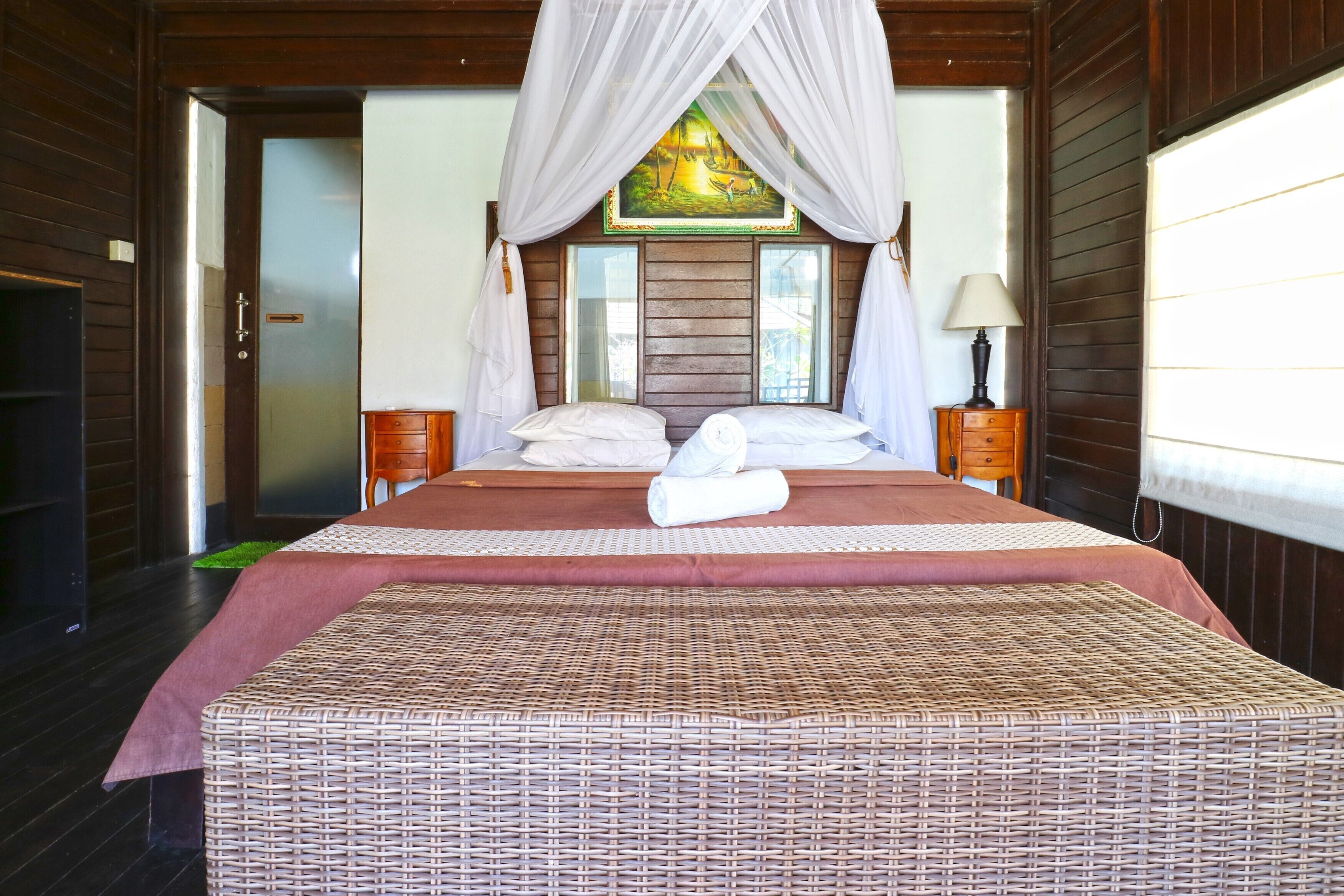 A spacious bedroom with a large bed, a wooden headboard, a painting above the bed, and a nightstand with a lamp.