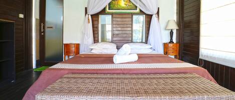 A spacious bedroom with a large bed, a wooden headboard, a painting above the bed, and a nightstand with a lamp.