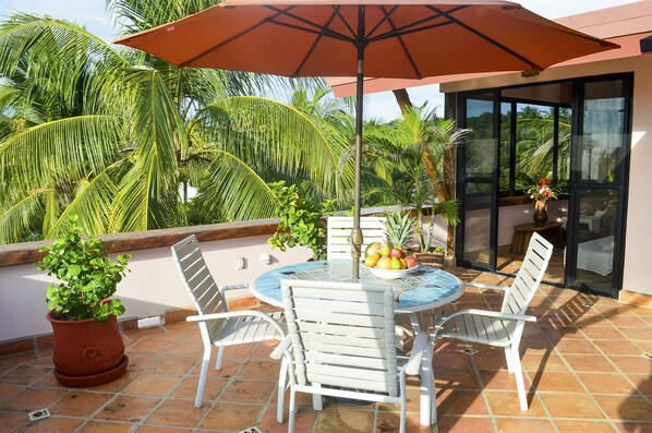Un patio con una mesa redonda, sillas blancas, una planta en maceta y un frutero.