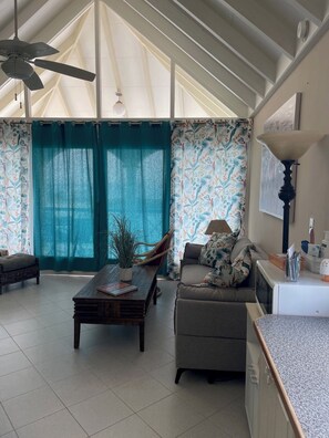 Ampla sala de estar com teto alto, ventilador de teto, mesa de jantar, sofá e área de cozinha.