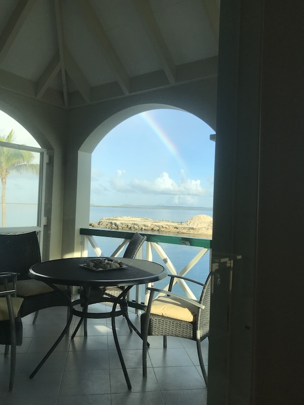 Uma área de estar coberta ao ar livre, com mesa e cadeiras, com vista para a praia e o mar.