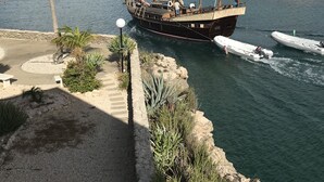 Un grand voilier était amarré dans une marina, le long d’une côte rocheuse bordée de palmiers.