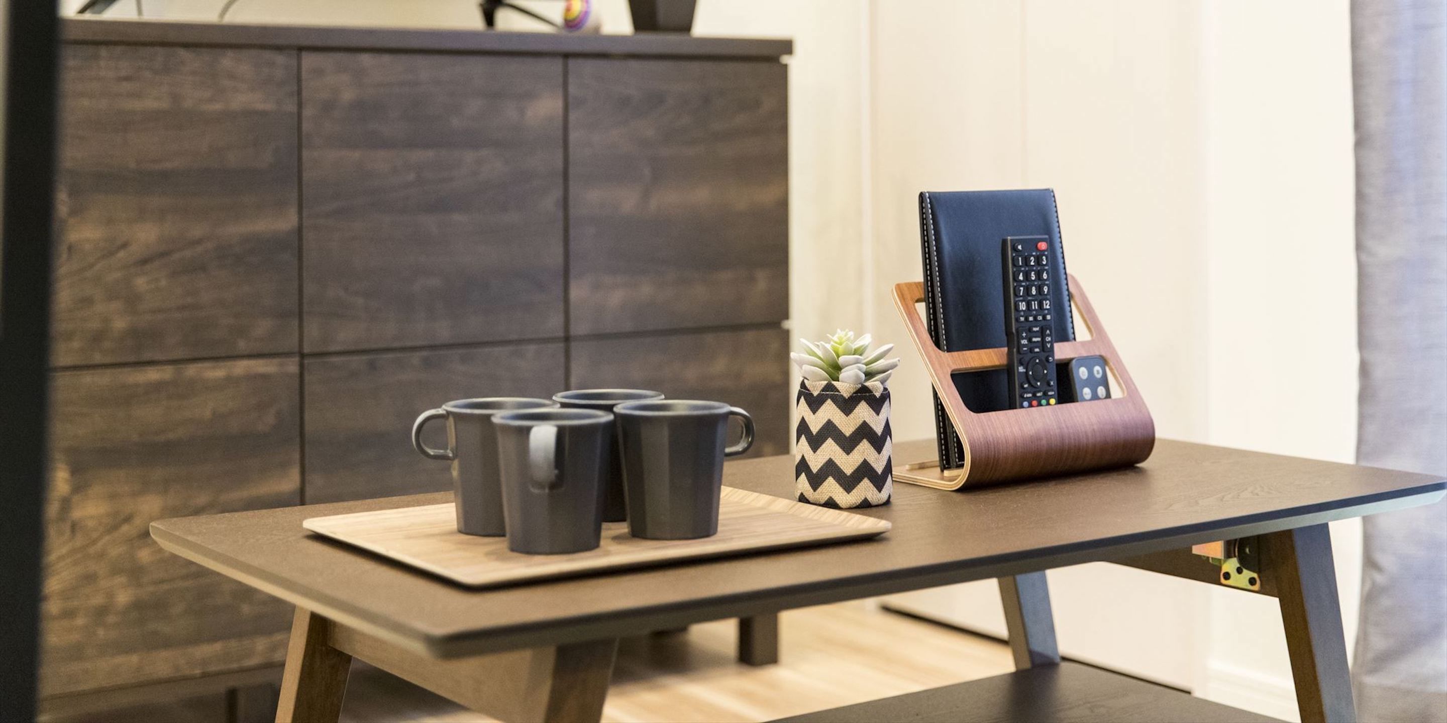 Una mesa con cuatro tazas negras, una pequeña planta en maceta y un original soporte para teléfono.