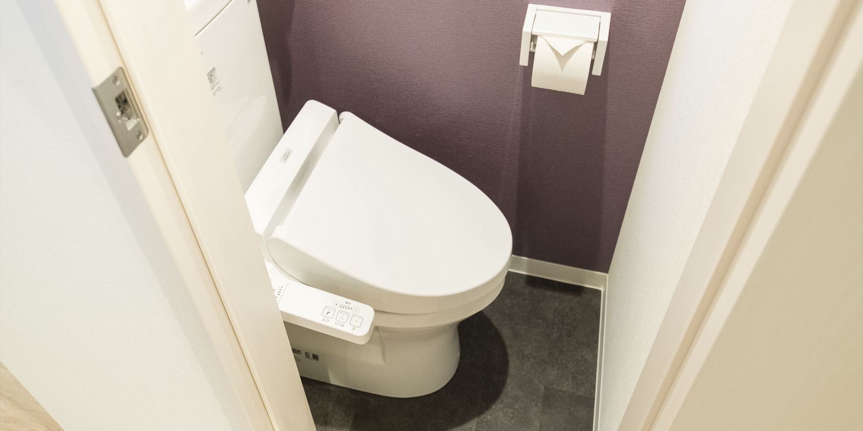 Un baño pequeño y moderno con un inodoro blanco, un dispensador de papel higiénico en la pared y una toma de corriente visible.