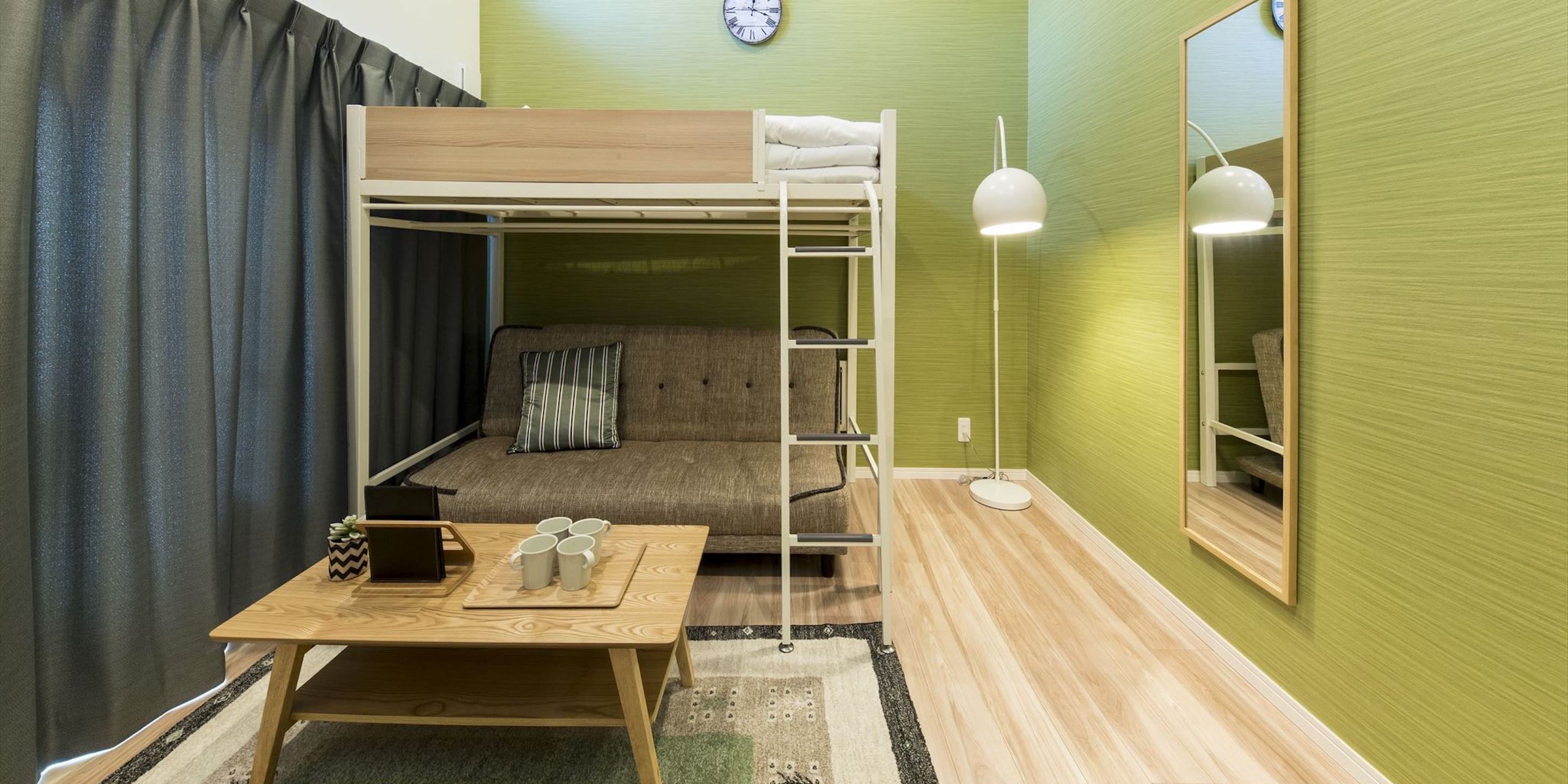 Una habitación con literas, una mesa de madera, un sofá, una lámpara y un reloj en la pared.