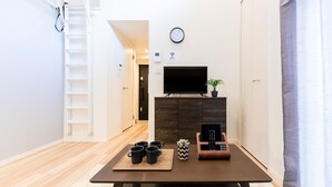A modern living room with a flat-screen TV, a coffee table with mugs, a remote control holder, and a potted plant. - Trip Pod Minoshima A (Fukuoka)