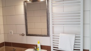 Une salle de bain avec un lavabo blanc, un miroir, un porte-serviettes et un support à papier toilette.