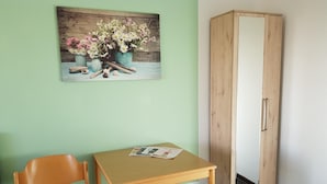 Une pièce avec une chaise en bois, une petite table sur laquelle repose un magazine, et une armoire en bois adossée à un mur vert.