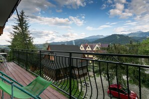 Un balcon doté d’une terrasse en bois, d’une rambarde en métal et d’une chaise verte.