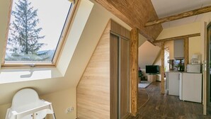 A modern loft with a sloped ceiling, a skylight, a wooden dining area, and a kitchen with a refrigerator and coffee maker. - VIP Apartamenty Widokowe (Zakopane)