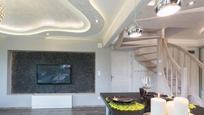 A modern dining area with a black table, white candles, and a TV mounted on a textured wall. - VIP Apartamenty Widokowe (Zakopane)