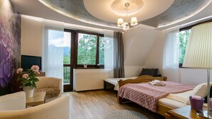 A bedroom with a bed, a desk, a chair, a radiator, and a window with a view of trees. - VIP Apartamenty Widokowe (Zakopane)