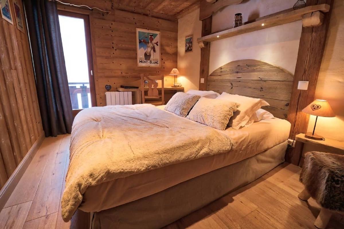 A cozy wooden room with a large bed, a wooden headboard, and a small table with a lamp.