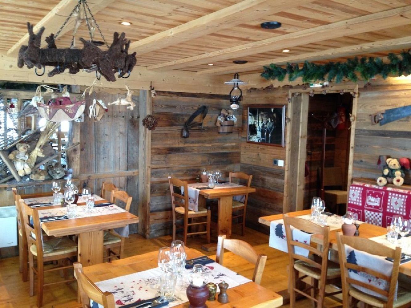 Un interior rústico de madera con varias mesas de comedor dispuestas para recibir a los invitados, con sillas de madera y diferentes tipos de vajilla.