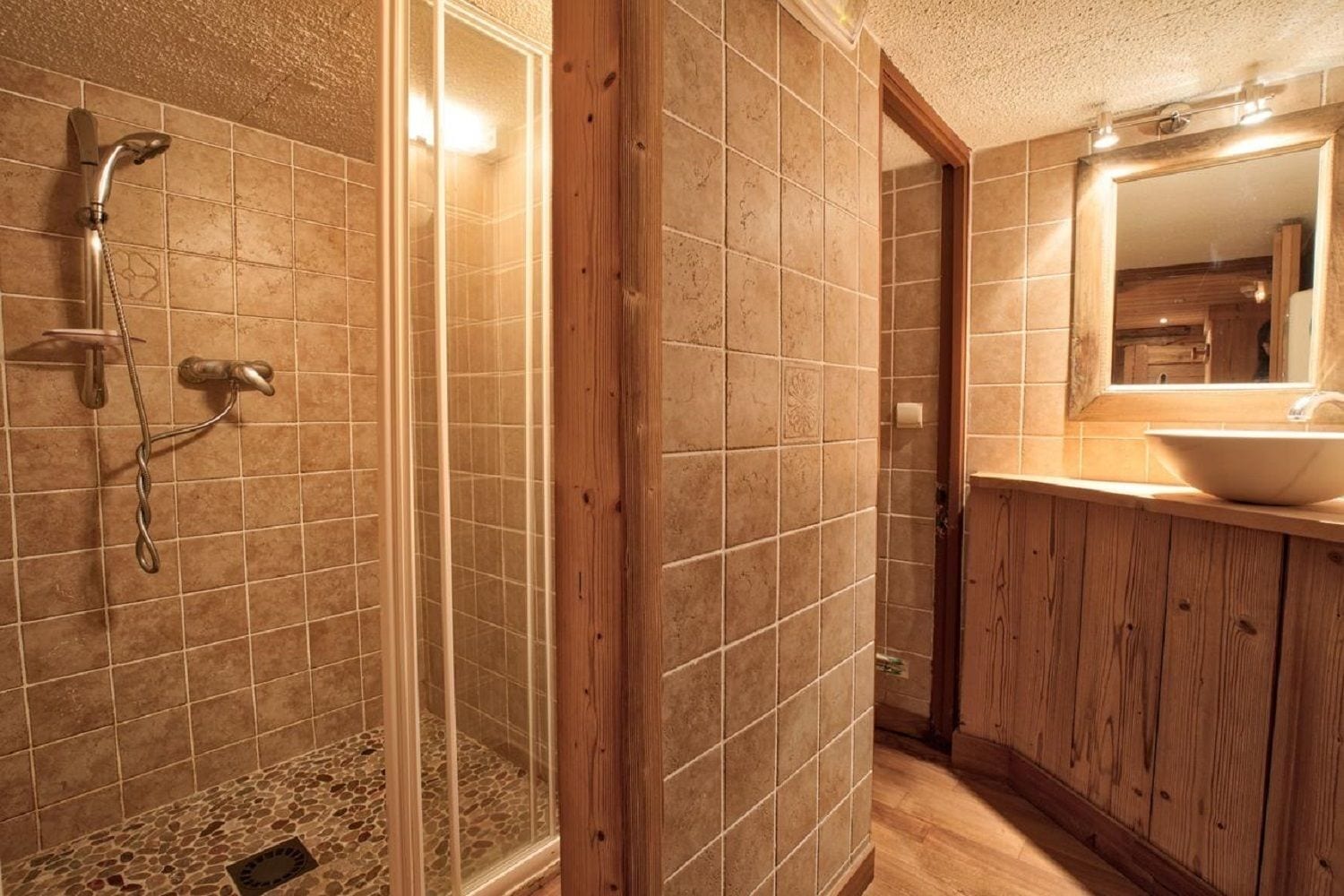 Un baño con ducha, paredes de azulejos, un mueble de tocador de madera y un espejo.