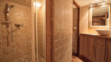 Un baño con ducha, paredes de azulejos, un mueble de tocador de madera y un espejo.