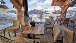A wooden deck with wicker chairs and a table, overlooking a snowy mountain landscape. - Chalet Hôtel du Mont Charvin (Cohennoz)