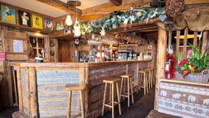 A rustic bar area with wooden stools, a bar counter, and various bottles and decorations. - Chalet Hôtel du Mont Charvin (Cohennoz)