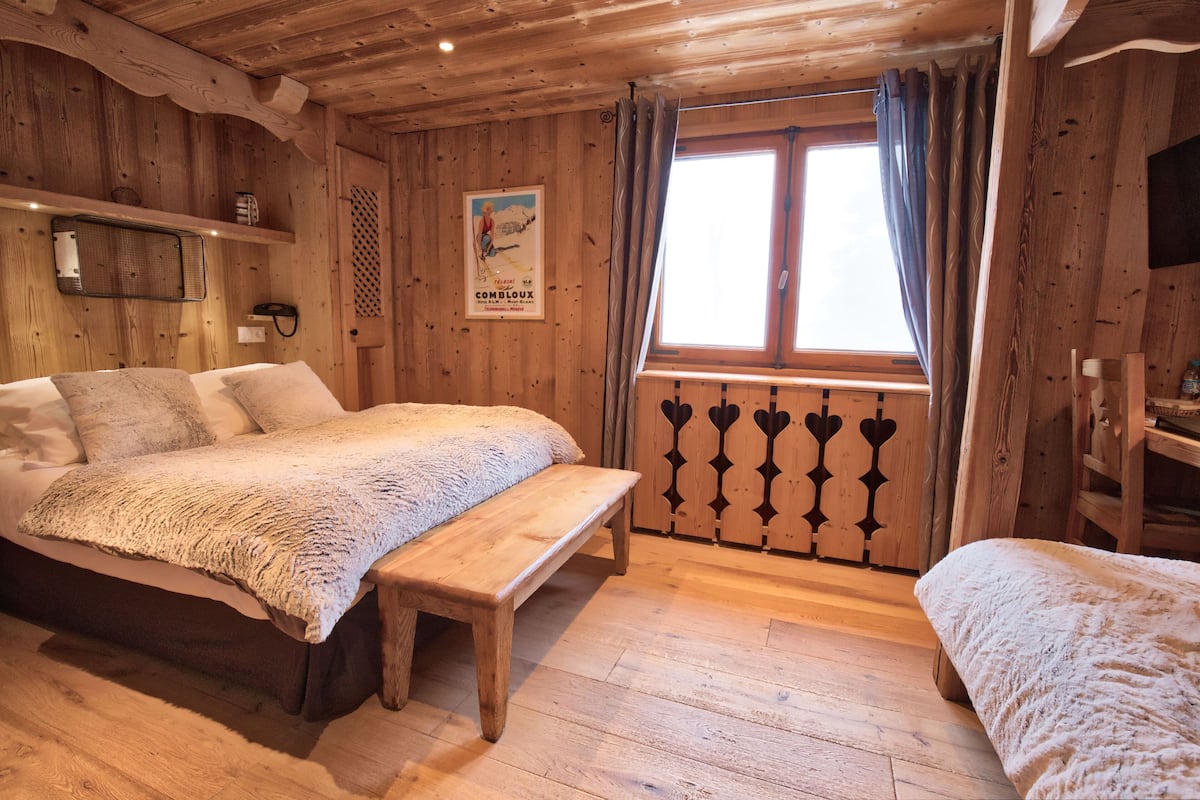 A wooden cabin room with a bed, bench, and window with curtains.