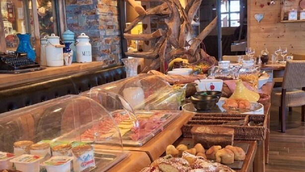 A buffet with various food items, including pastries and desserts, in a rustic setting with wooden decor and a brick wall. - Chalet Hôtel du Mont Charvin (Cohennoz)