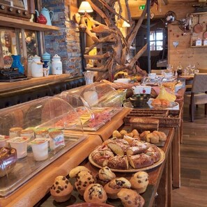 A buffet with various food items, including pastries and desserts, in a rustic setting with wooden decor and a brick wall. - Chalet Hôtel du Mont Charvin (Cohennoz)