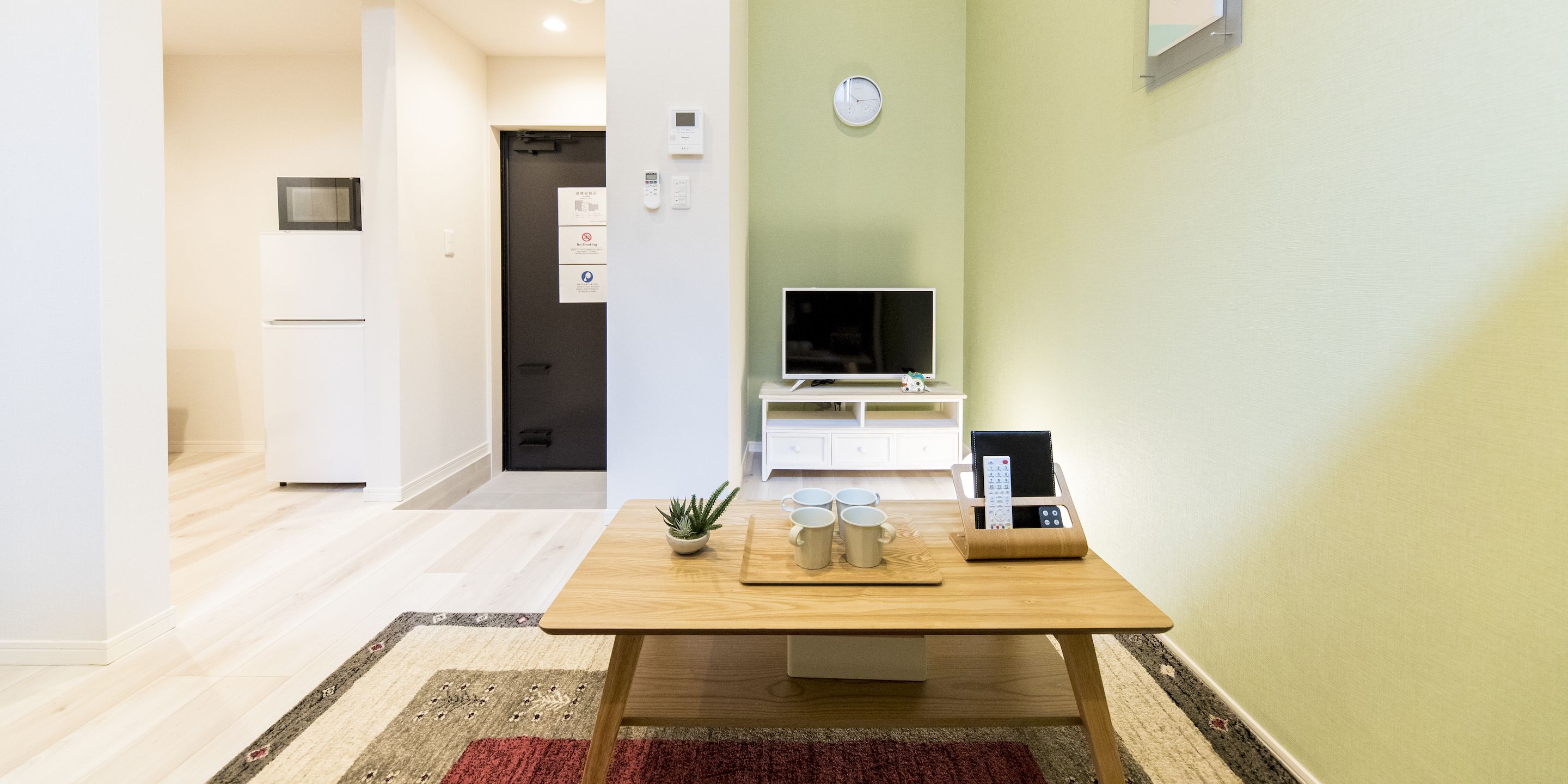 A modern living room with a wooden table, a small plant, and a TV on a white stand.