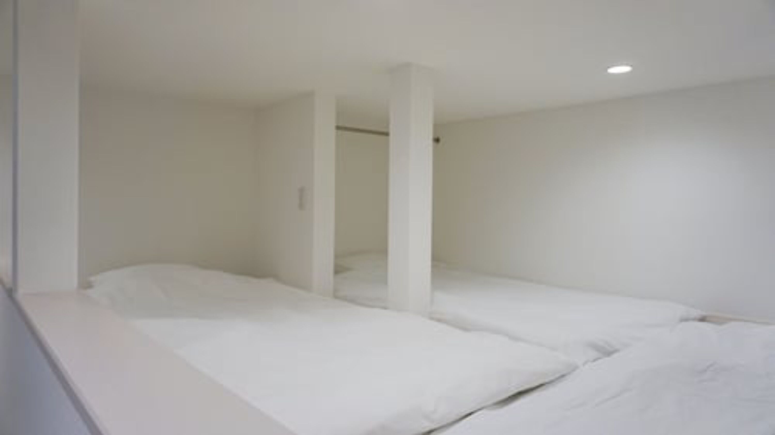 A minimalist room with two single beds, white walls, and a simple, clean design.