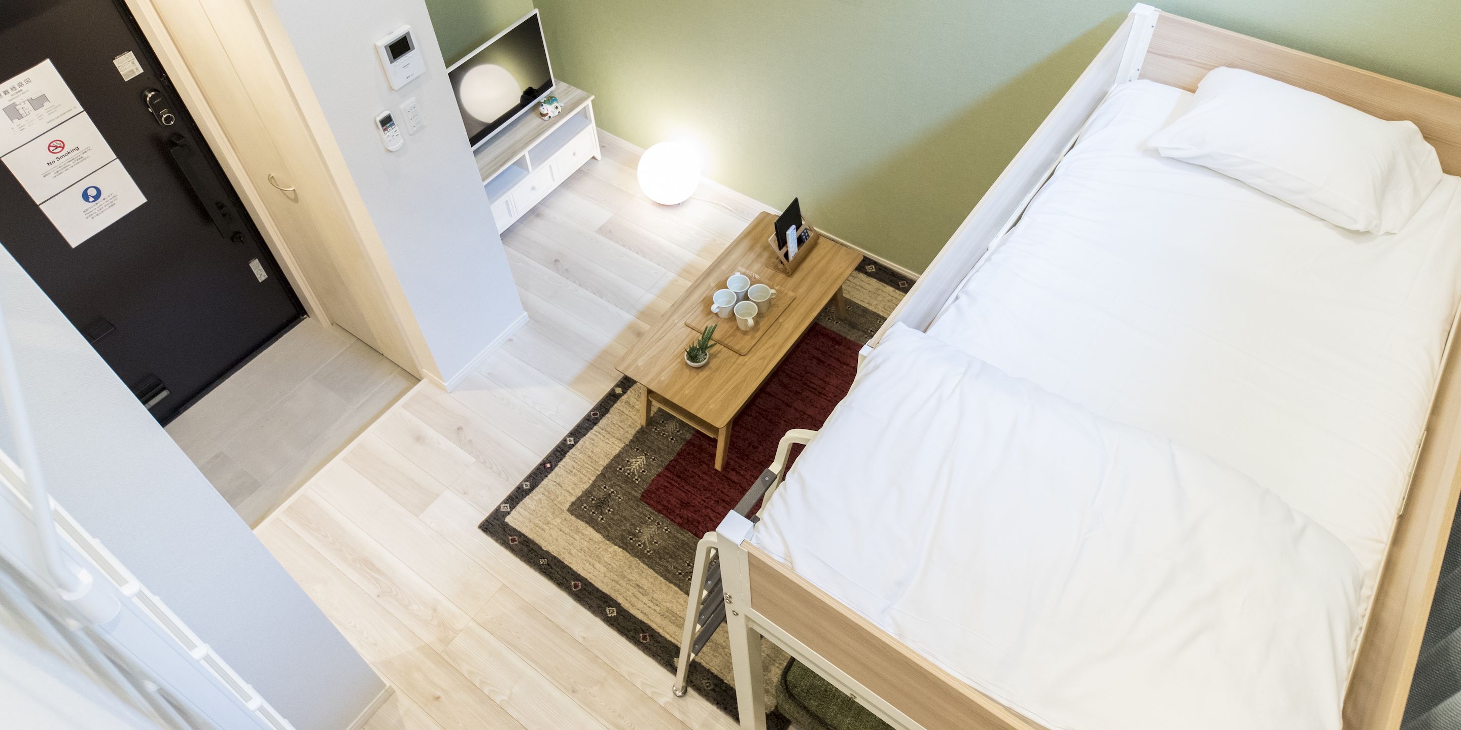 A small, single-bed room with a wooden bed, a bedside table with a lamp, and a small rug.