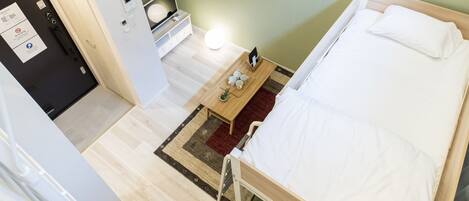 A small, single-bed room with a wooden bed, a bedside table with a lamp, and a small rug.