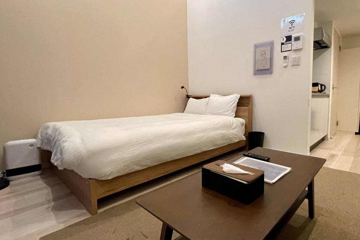 A single bed with a wooden frame and white bedding, a bedside table with a remote control and a tissue box, and a wall-mounted Wi-Fi sign.