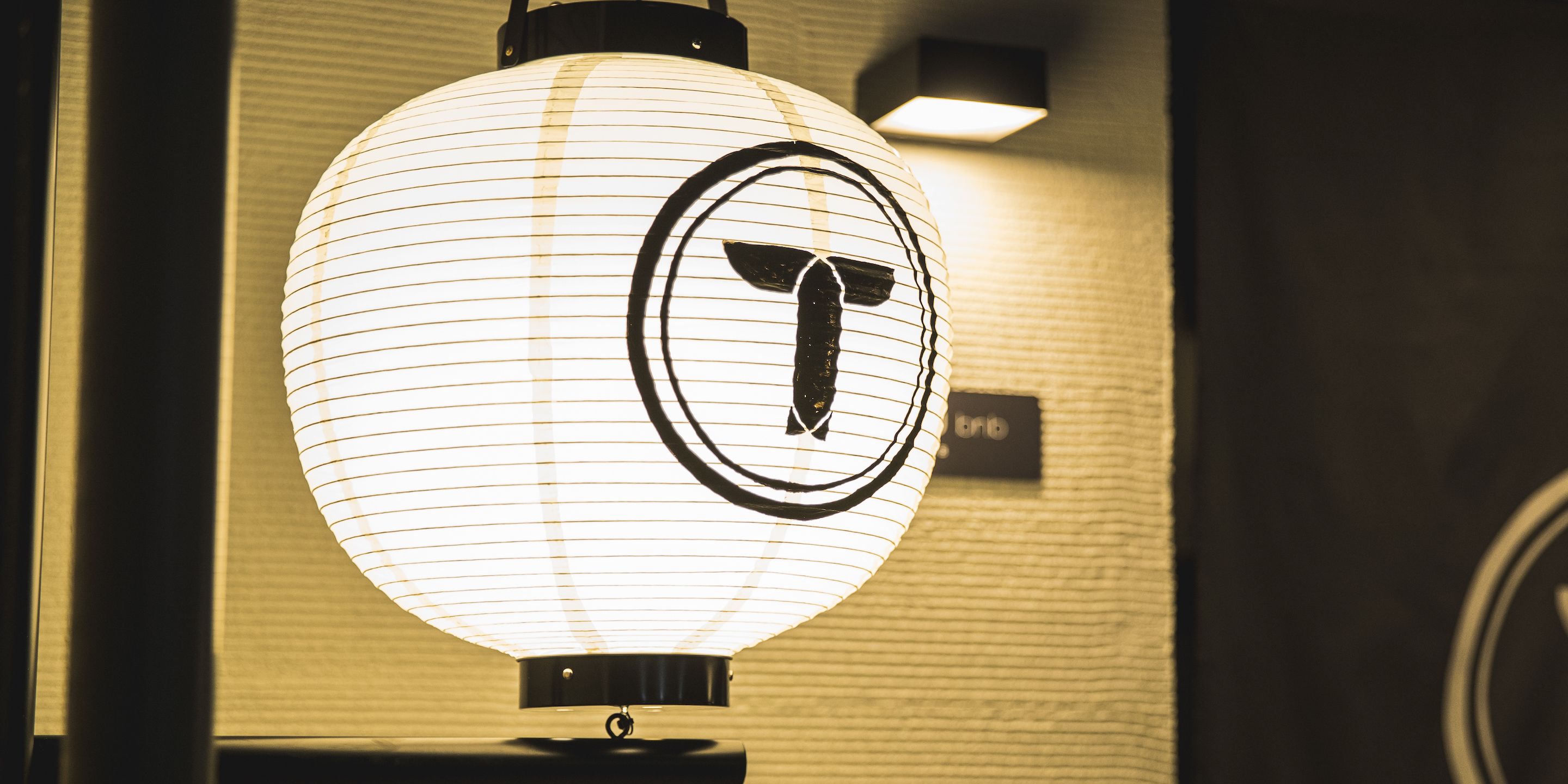 A white, round, illuminated sign with a black logo, mounted on a wall with a textured surface.