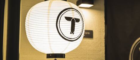 A white, round, illuminated sign with a black logo, mounted on a wall with a textured surface.
