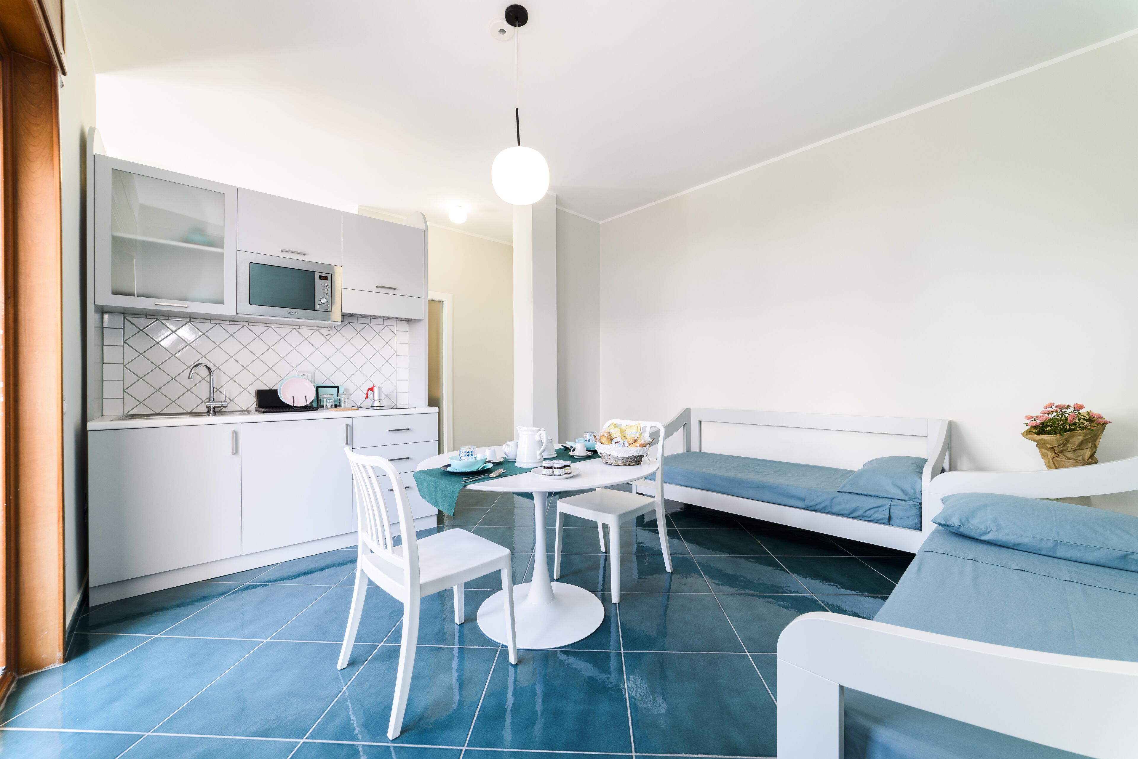 A compact room with a kitchenette, a dining table with chairs, and a bed with blue bedding.