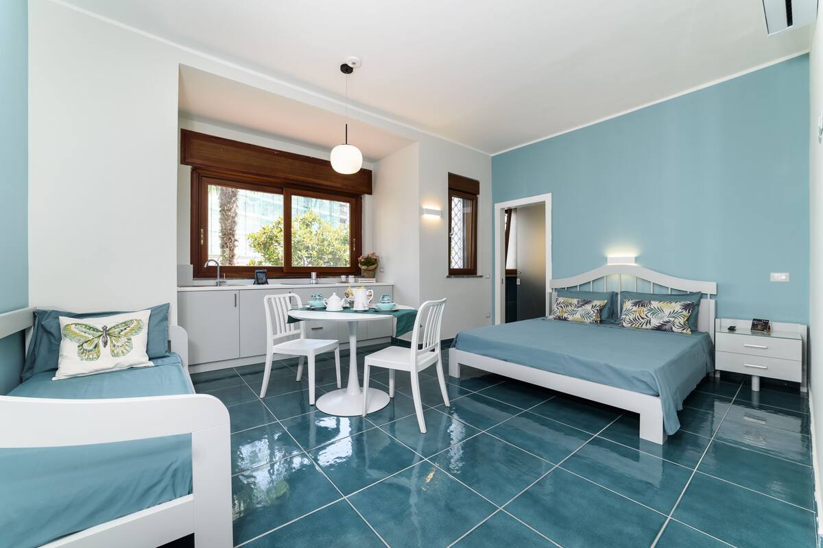 A modern bedroom with a bed, a dining table with chairs, and a kitchenette area.