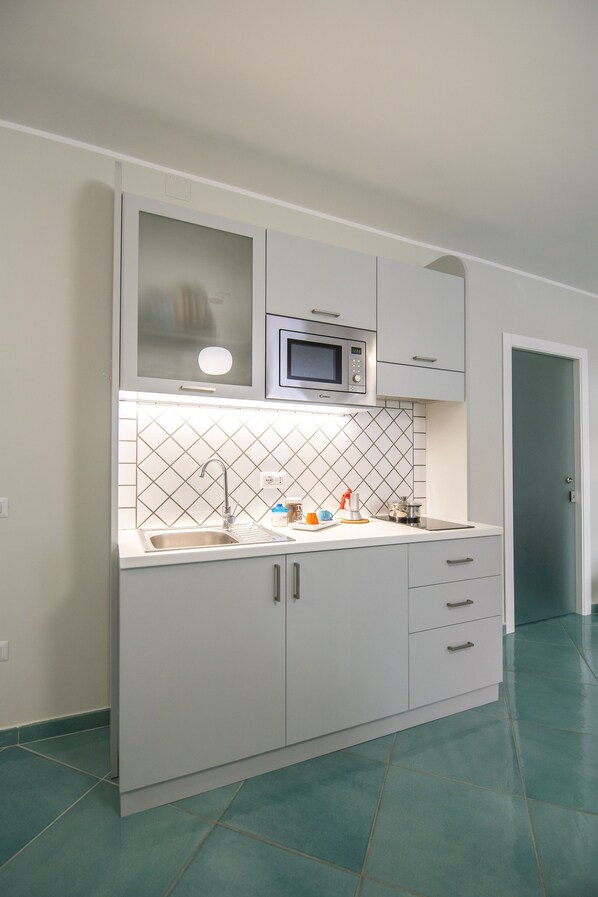 Una cocina moderna con armarios blancos, un lavamanos de acero inoxidable, un microondas y un salpicadero de azulejos.