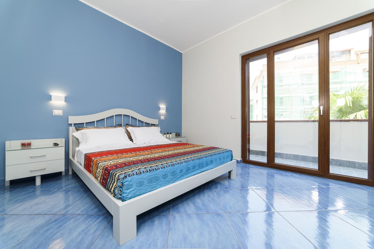 A bedroom with a bed, a nightstand, a window with a view, and a door.