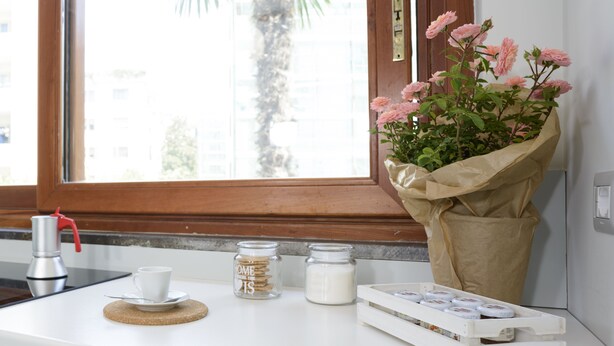 Una encimera de cocina con una cafetera, una taza, dos tarros y un ramo de flores.